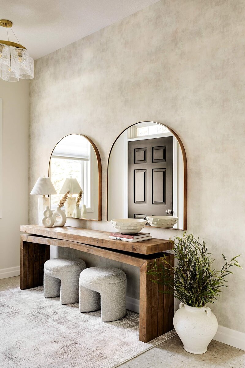 A foyer with a rustic wood console, ottomans and arched mirrors. 