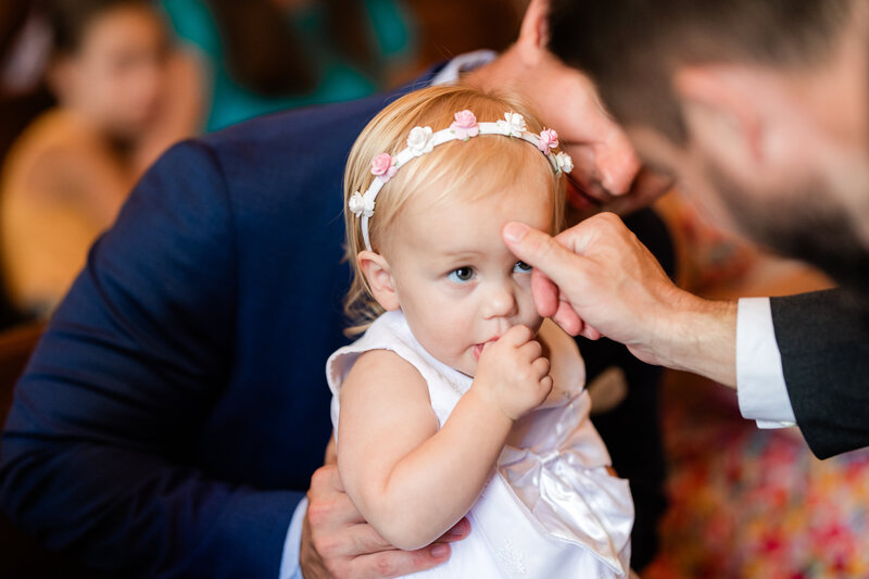 Toddler being baptize in white dress and flower crown.
