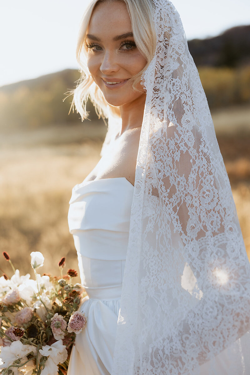 bridal portrait of a blonde bride with a veil and backlight from the sun in park city.