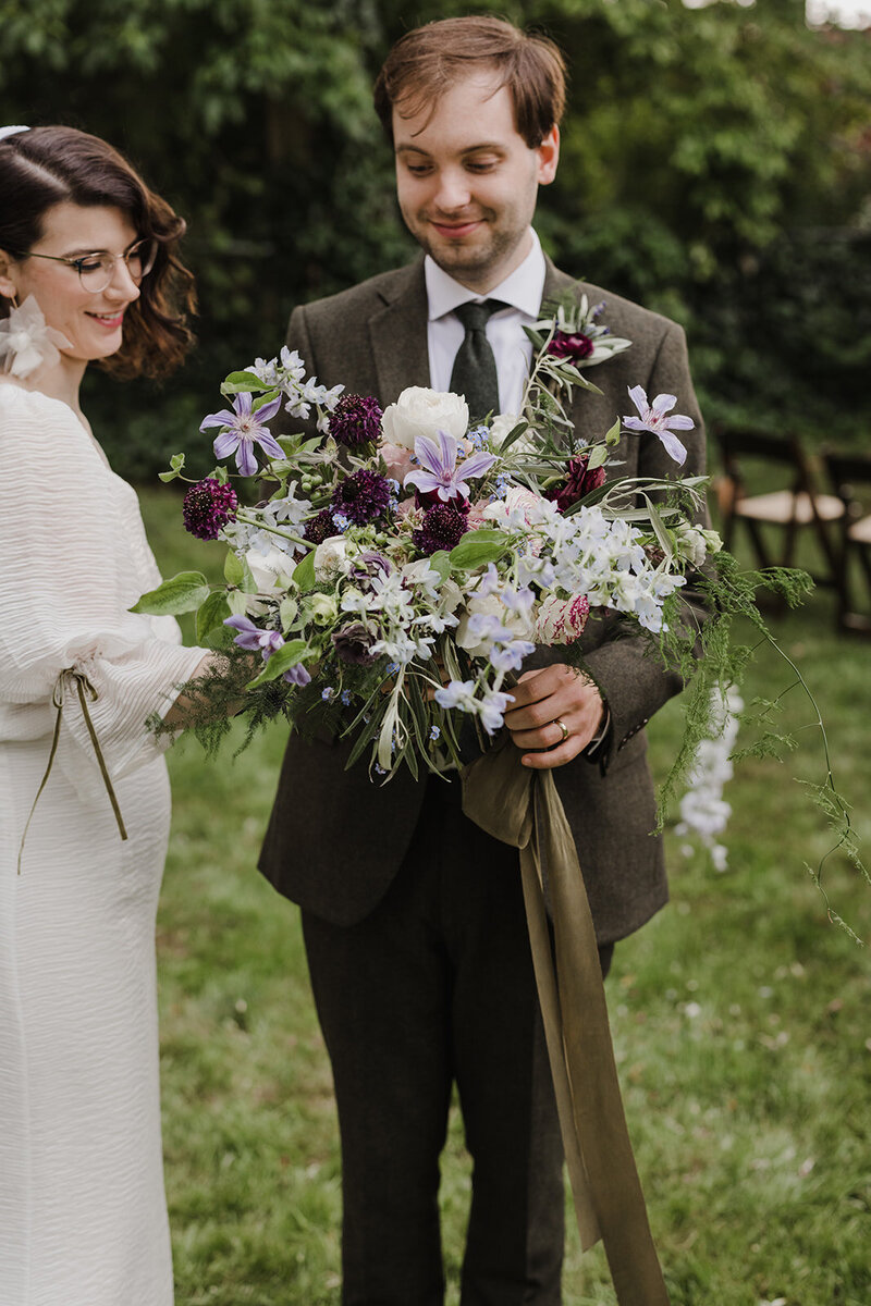 Bride and groom looking at wedding bouquet of purple, ivory and burgundy florals by Jessamine floral and events, New Jersey and Philadelphia