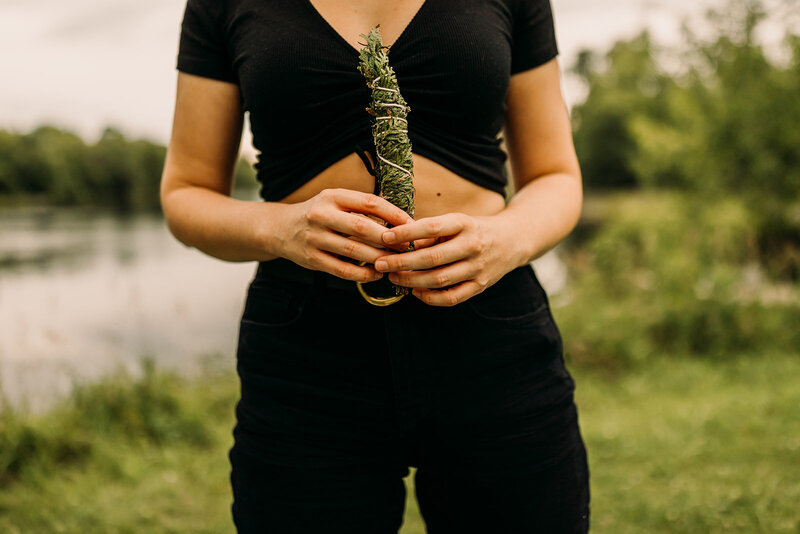 A woman holds a bundle of greenery in front of her torso.