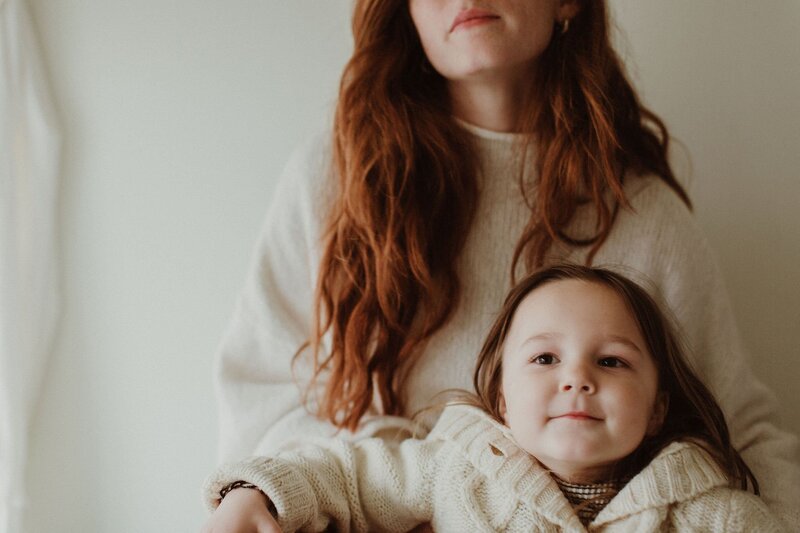 mother and daughter snuggled up in cozy white winter sweaters