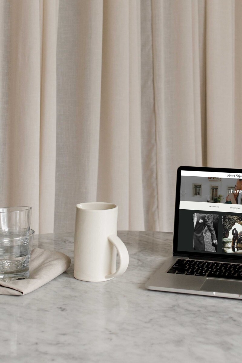 A laptop sits on a table by cups.