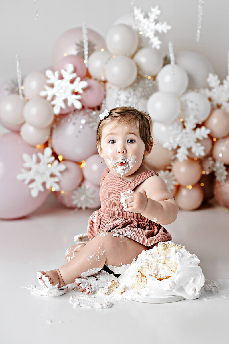 Toddler girl smashing a cake with a wooden spoon with a big open mouth smile.
