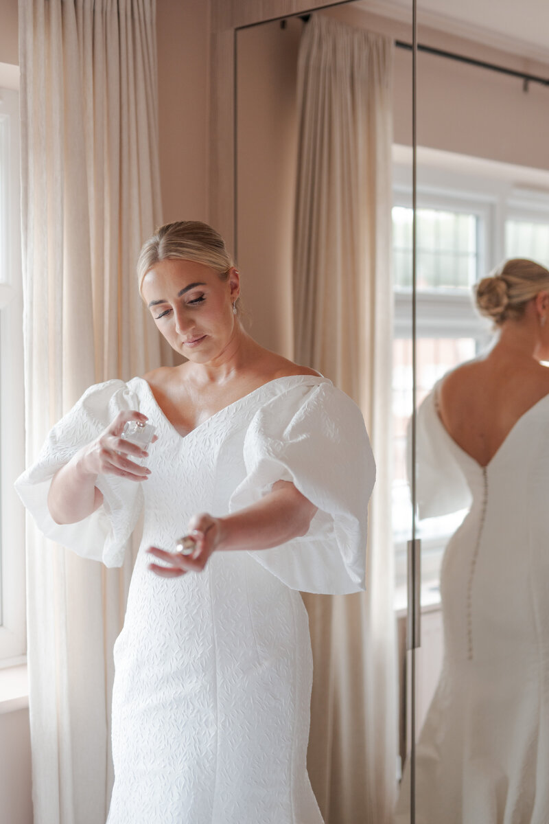 Bride applies her perfumed next to a mirror.