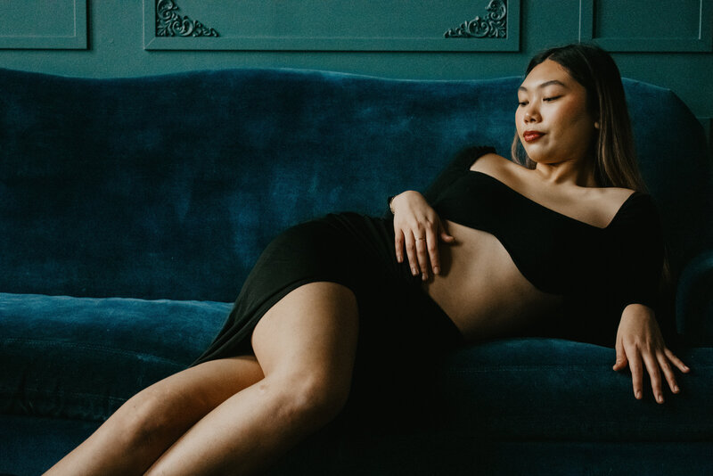 Woman lounging on a dark blue velvet wall in a two piece cut out dress.