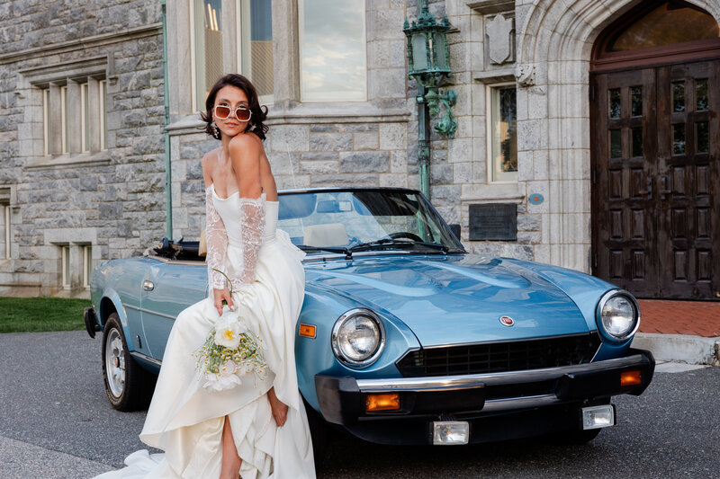 A Bride posing with an antique car in front of the Branford House at Avery Point In Connecticut.