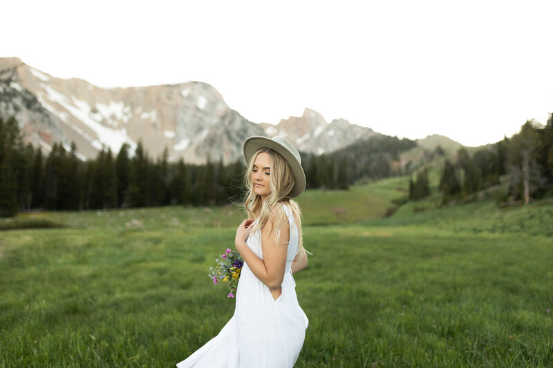 High school senior twirls in the mountains as she holds a wildflower bouquet.
