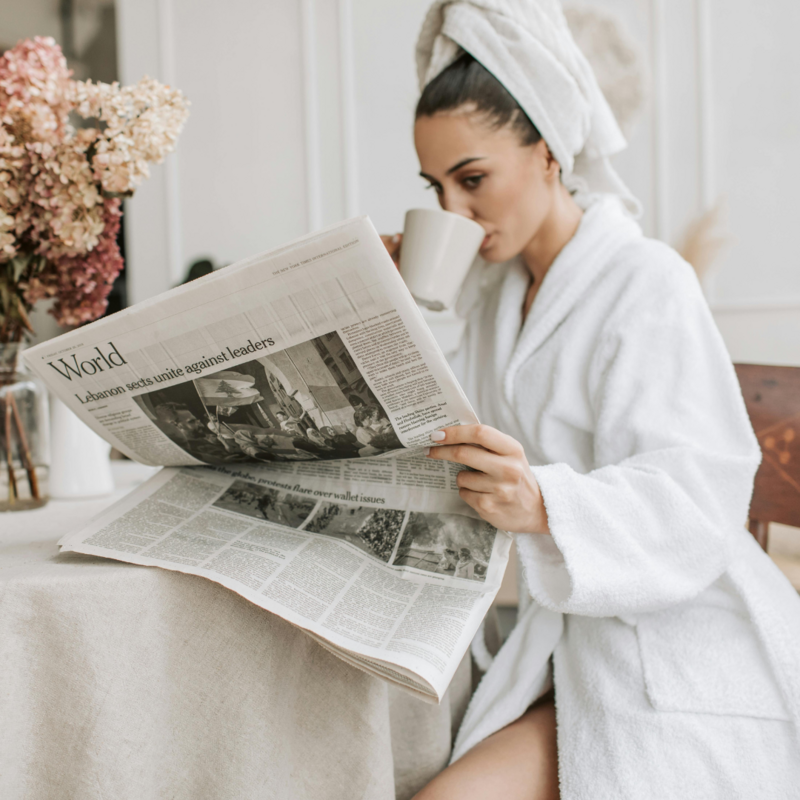 woman in robe and towel reading newspaper and drinking coffee