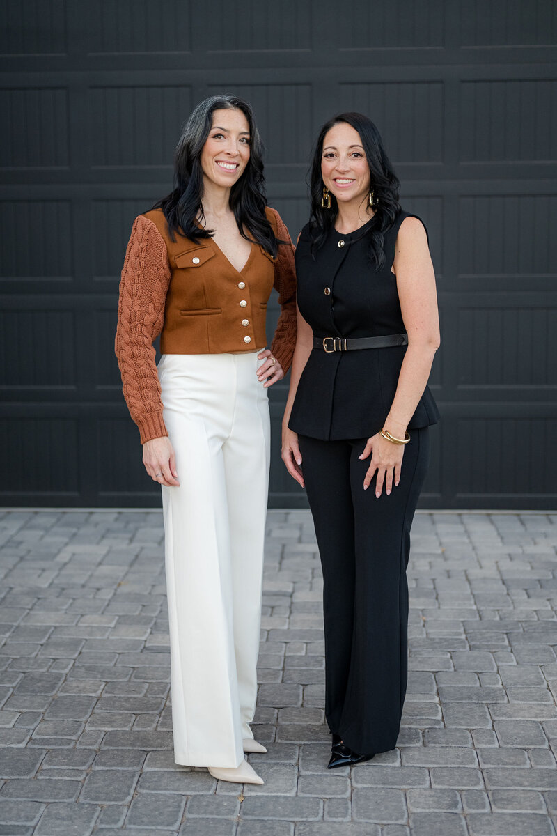 Two women standing by a garage door, engaged in a conversation about sales methodologies and performance improvement.