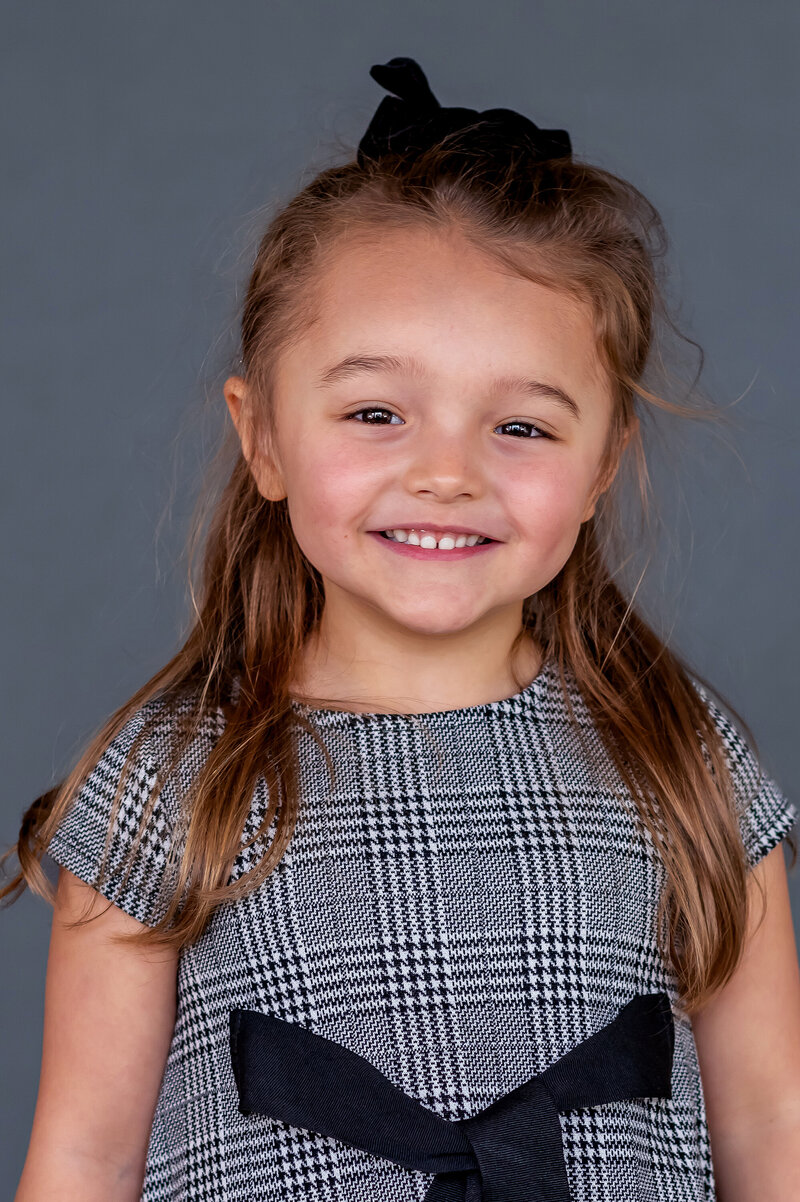 Preschool girl in black and white plaid dress smiling for her school photo