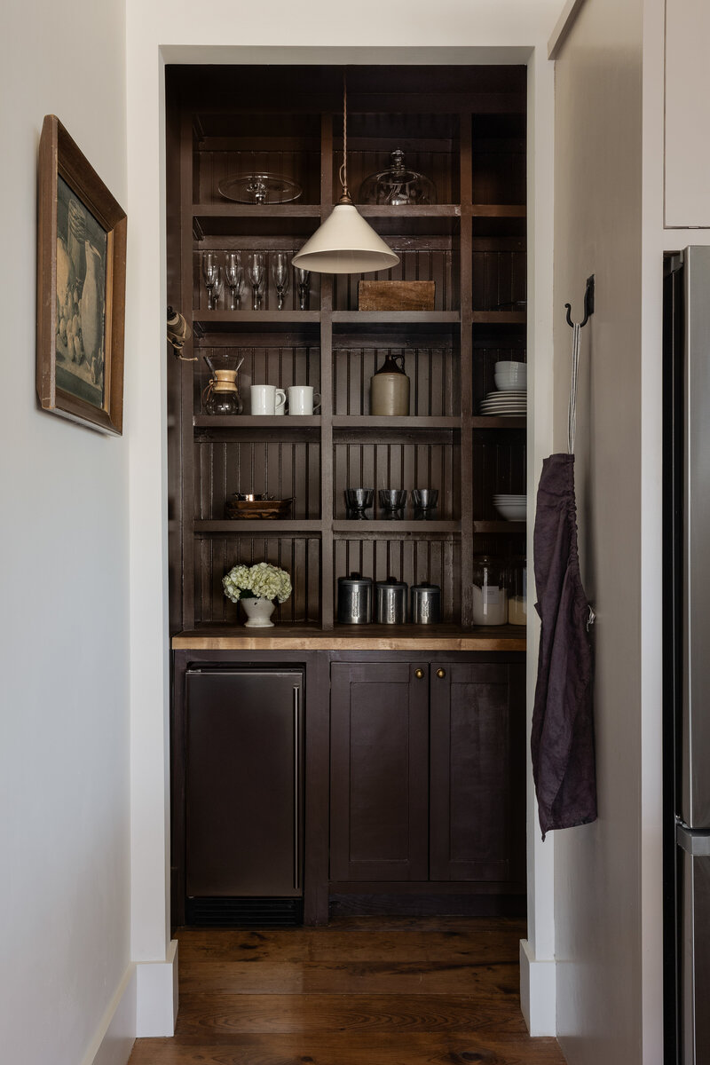 Deep chocolate browns, old world trim, and a hand-made ceramic pendant light bring this butler's pantry to life by Jessa Myer Interiors.