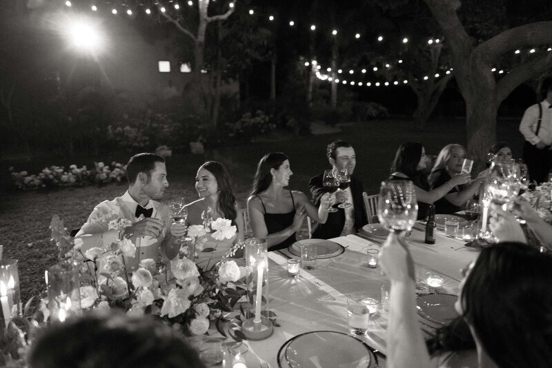Black and white photo of bride and groom and bridal party at reception table under string lights