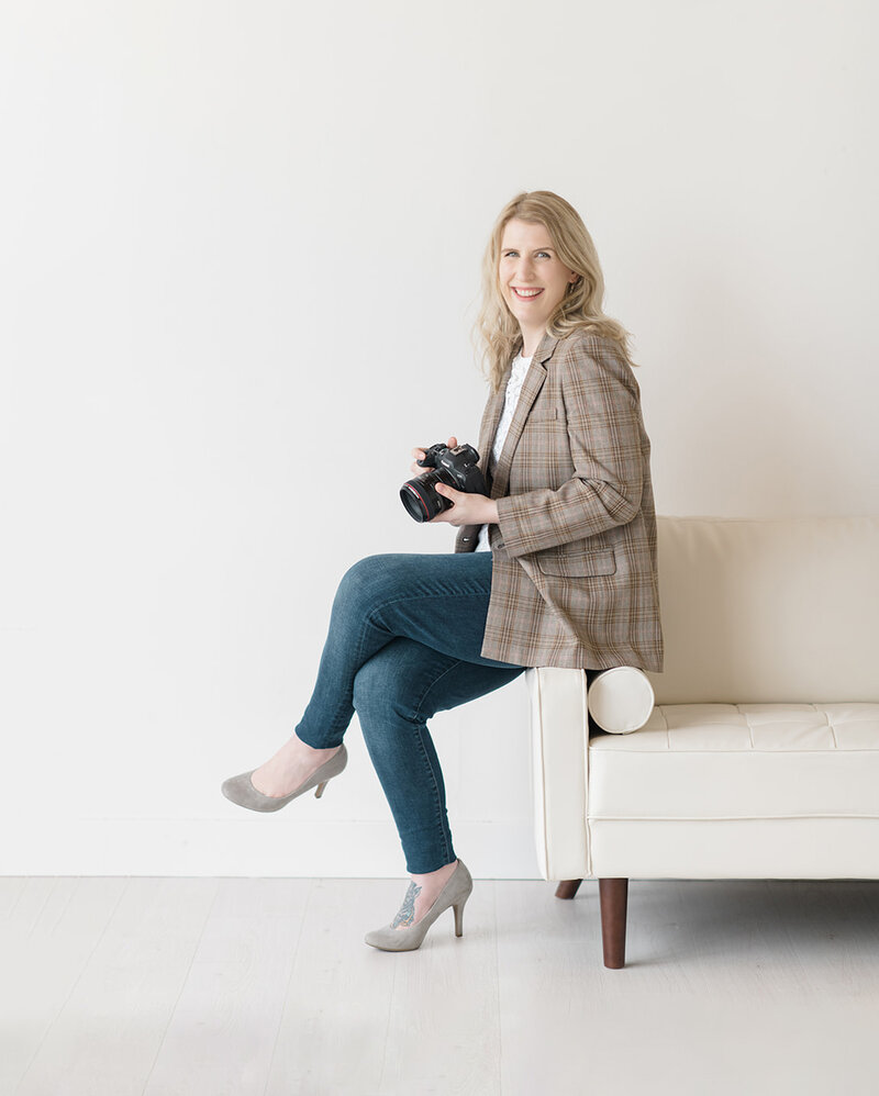Photo of Shaunae Teske, a wedding photographer in Seattle, wearing a plaid blazer looking down at her camera and smiling while sitting on a stool