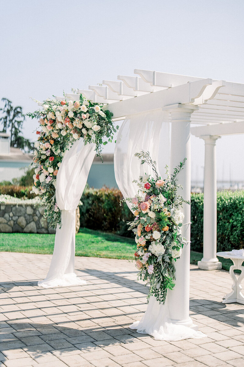 A stunning California wedding set against the rugged cliffs and serene ocean backdrop. The bride and groom share a private moment on a cliffside, surrounded by the natural beauty of the California coast. The bride’s flowing gown contrasts beautifully with the vibrant green and earthy tones of the cliffside, while the peaceful ocean waves crash below. This breathtaking coastal location encapsulates the romance and majesty of a dream California wedding.