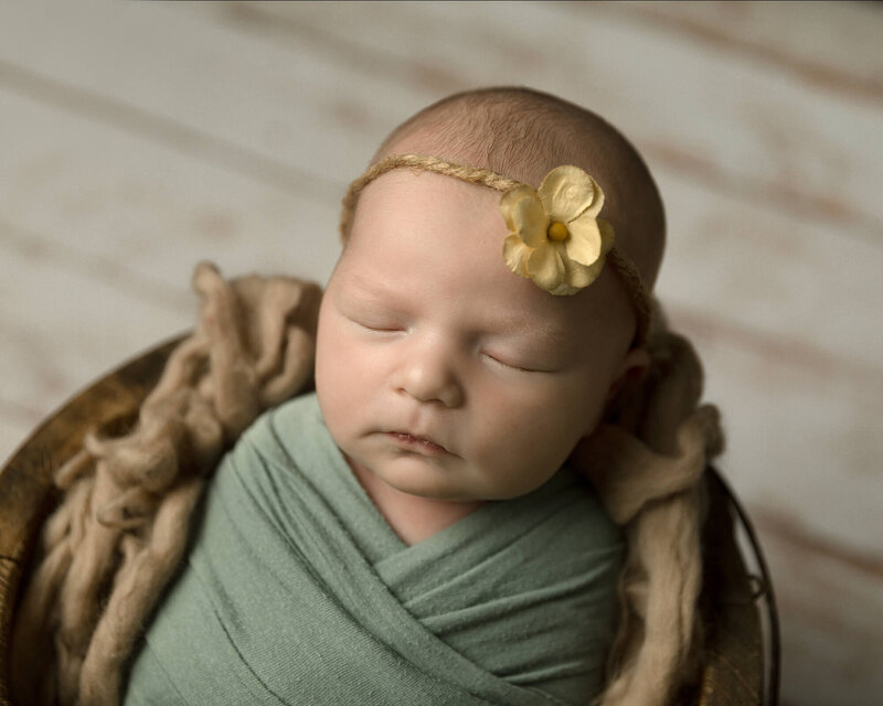 Newborn girl sleeping with green wrap and yellow flower headband.