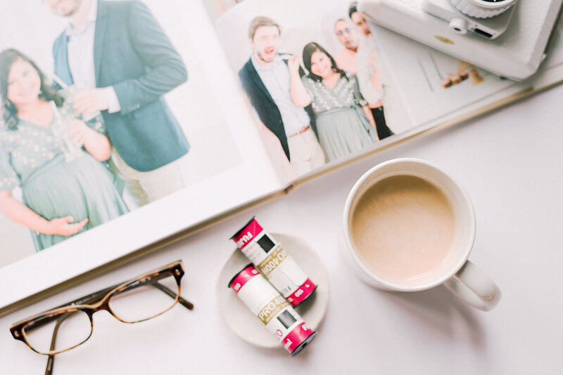 Open wedding album set on a table next to glasses, rolls of film, and a cup of coffee