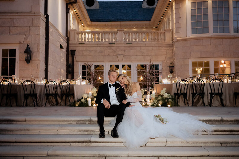 bride and groom sitting on steps outside utah wedding venue at dusk