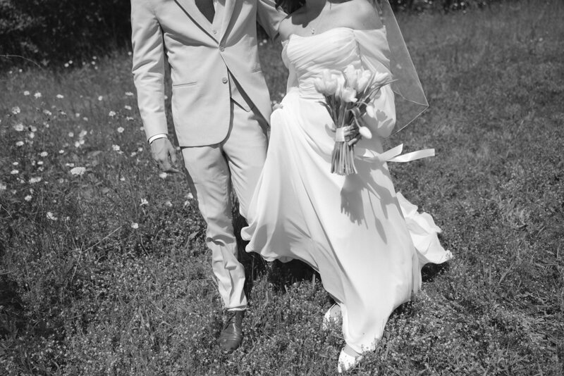 Black and white image of bride and groom walking through grassy field at Nashville wedding