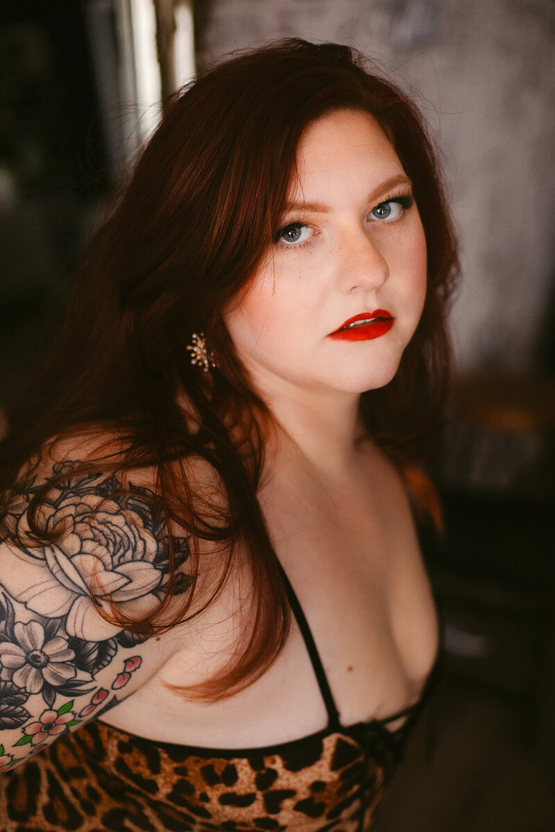 A woman with red hair looks seductively at the camera during a Bentonville boudoir photoshoot.