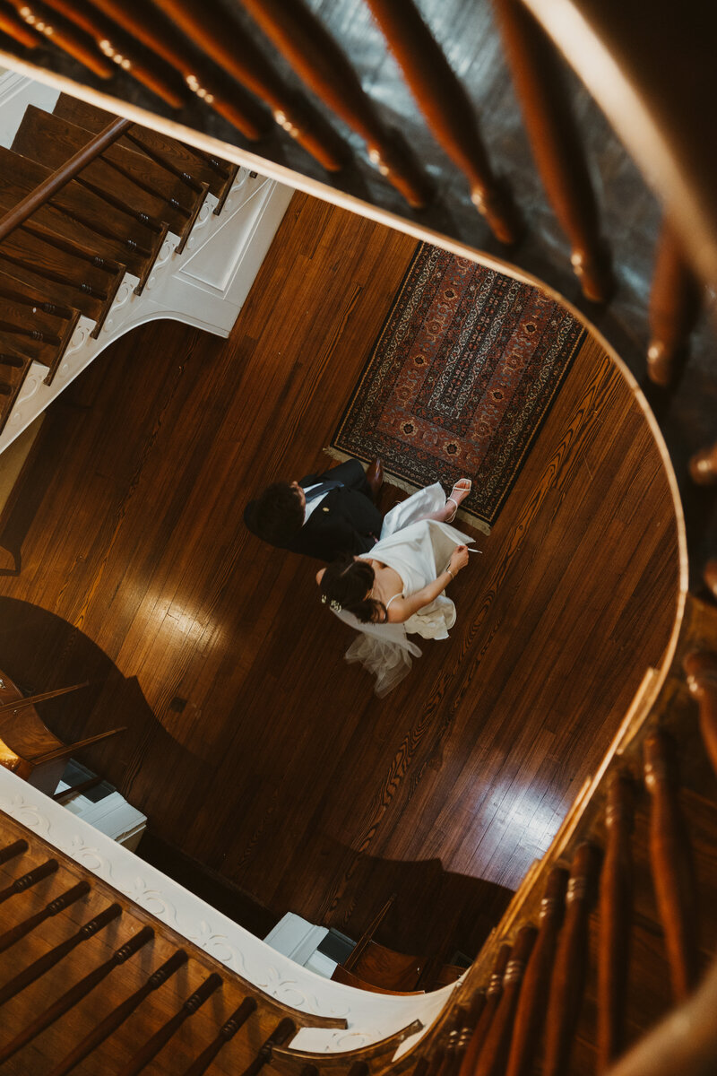 bride and groom walk hand in hand under staircase