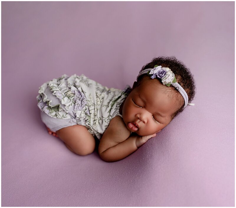 Portrait of baby laying on purple backdrop with head on hands by brooklyn newborn photographer