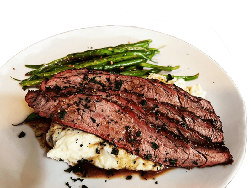 sliced beef brisket over mashed potatoes with green beans on a white plate