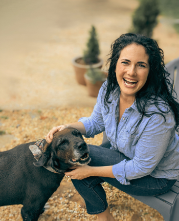 Women's life coach caroline busick sitting outside on a  patio with her dog laughing