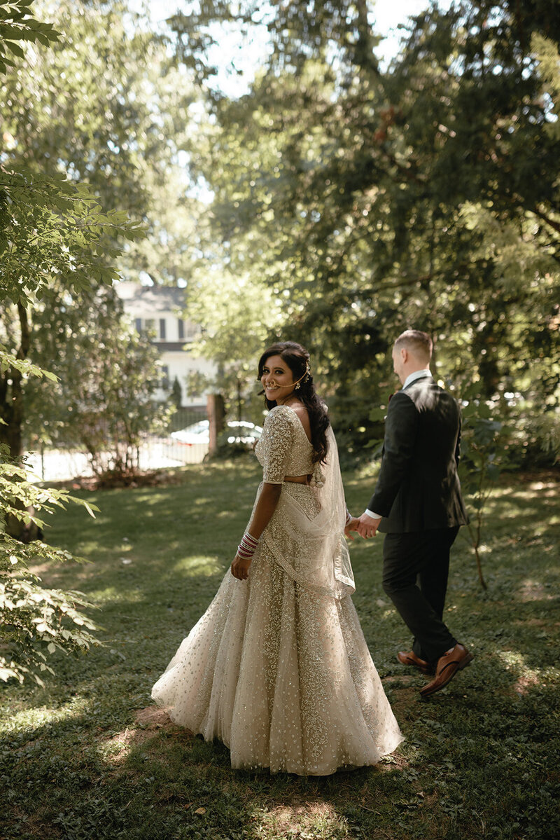 A romantic, intimate garden wedding in Glen Ridge, NJ, featuring the bride in a beaded champagne gown and the groom leading her through a sunlit pathway.