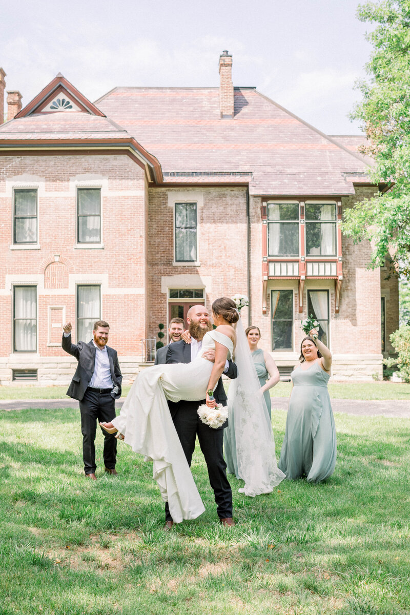 groom carrying bride with full bridal party cheering behind