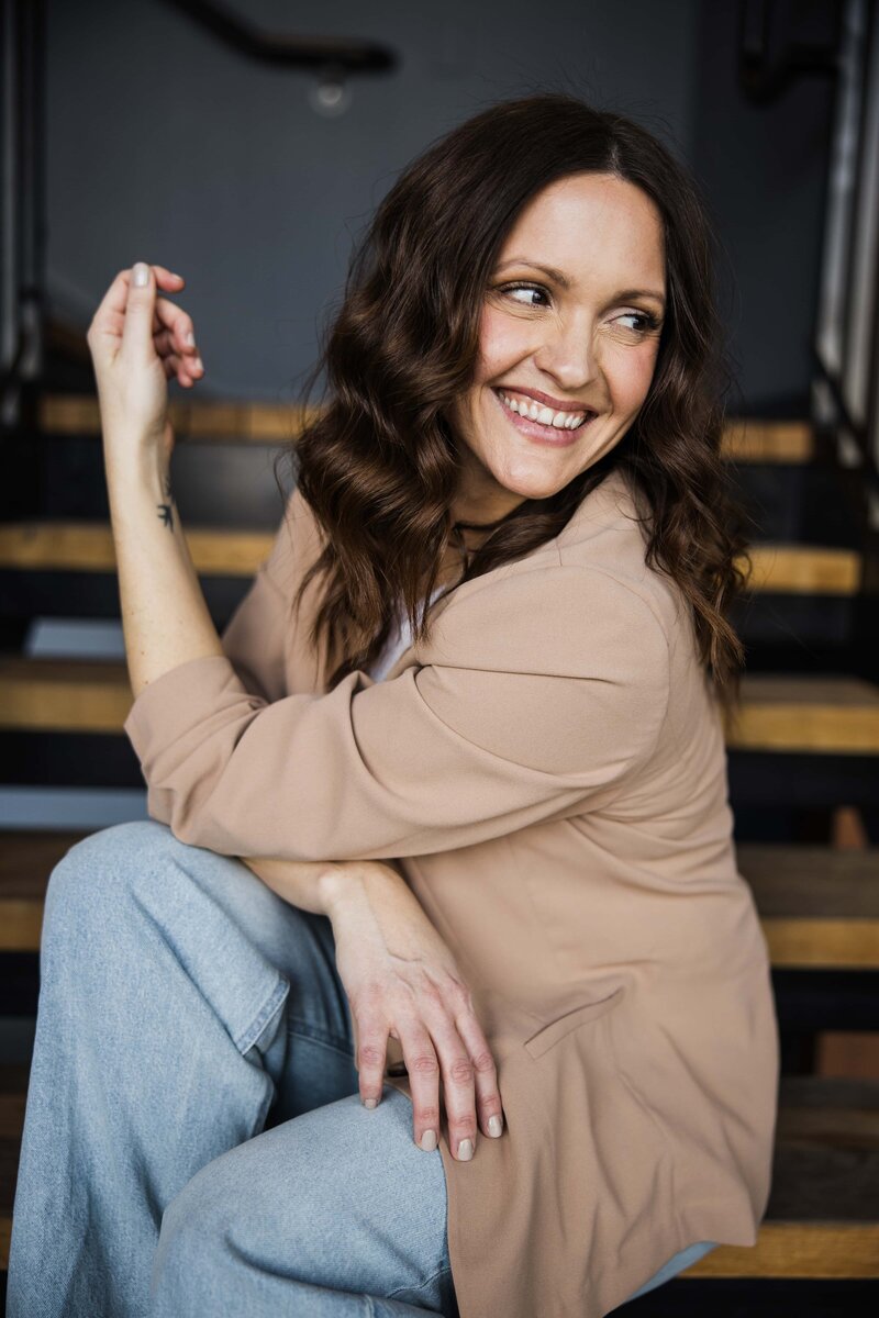 A smiling woman, participating in a photography mentoring program, holding a camera, seated in a cozy room with soft lighting.