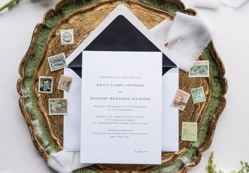 A captivating detail shot of a wedding invitation suite elegantly arranged with complementary colored stamps and a glass plate, captured in a flat lay photograph, showcasing intricate design and sophistication.