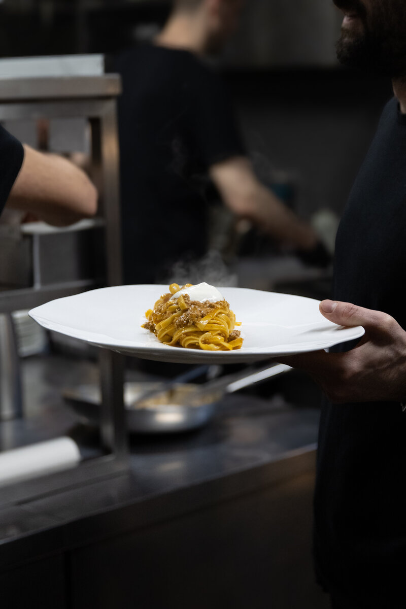 Fettuccini bolognese served on whit plate by server in kitchen