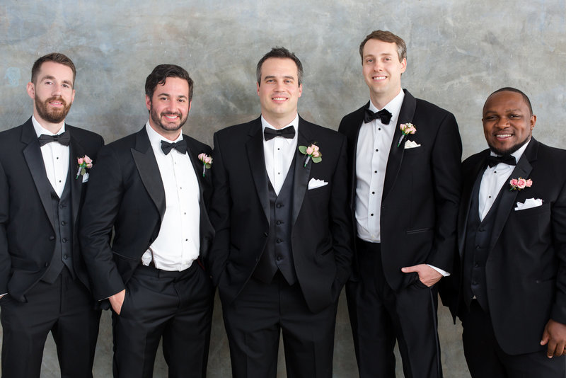 Groom and groomsmen stand together in black tuxedos