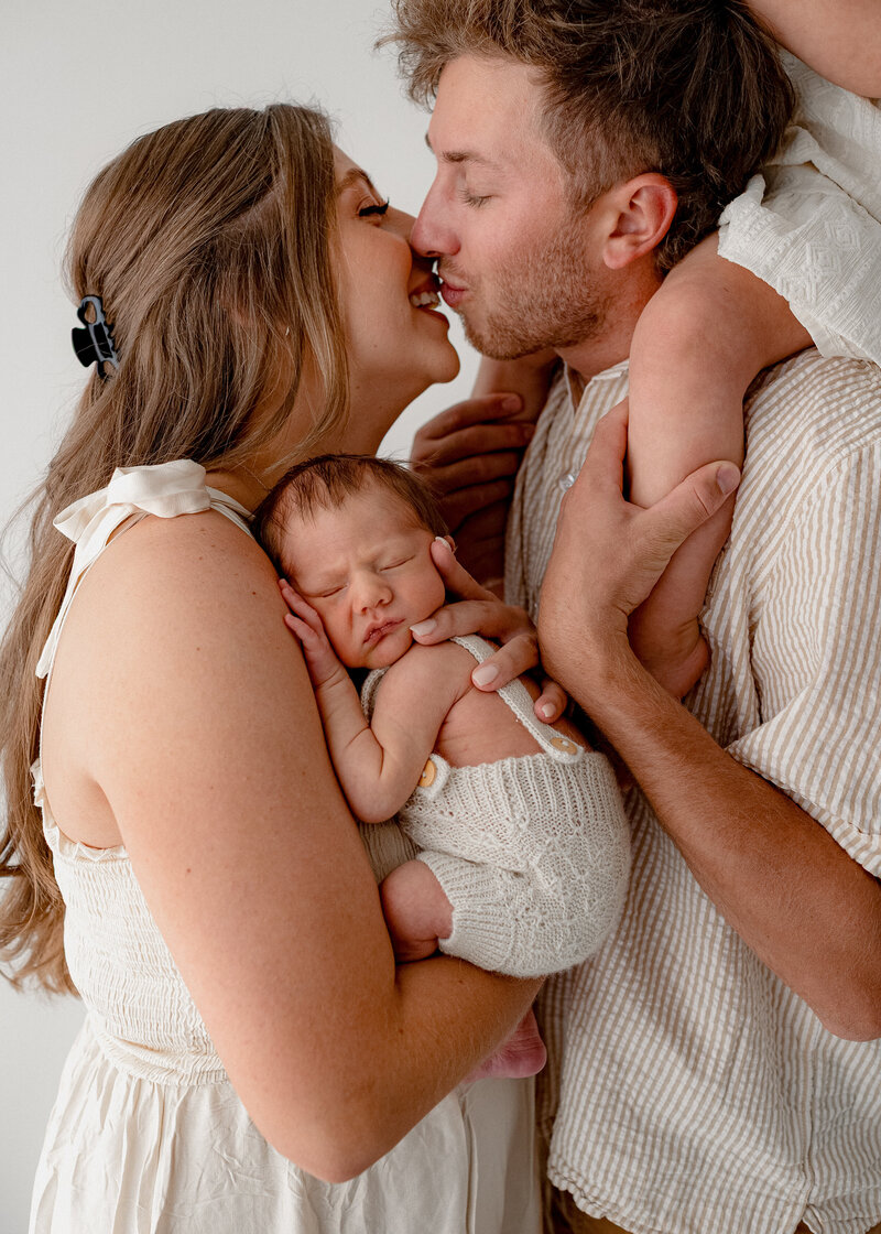mom and dad holding their daughter and giving her kisses during their family photoshoot in erie colorado at sunset