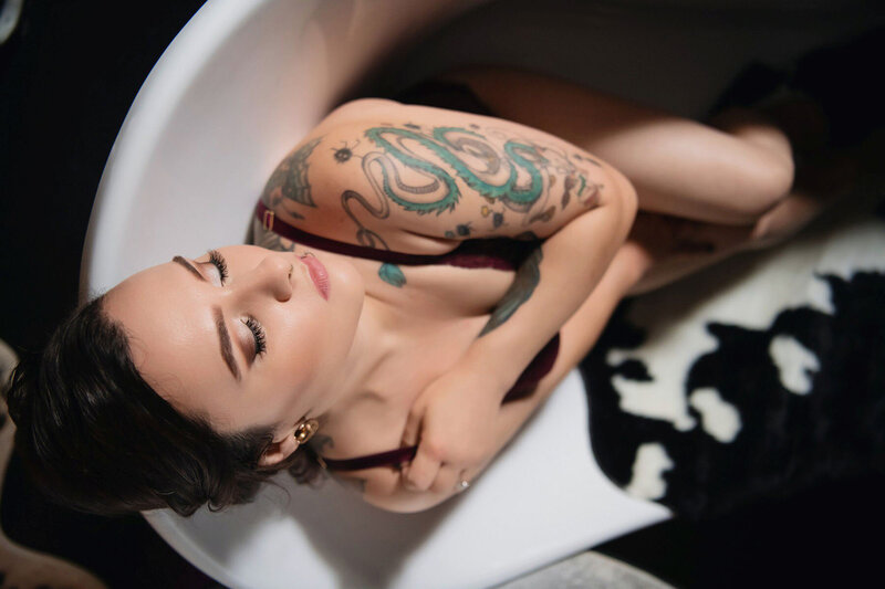 Tattooed woman posing in bathtub for boudoir photoshoot