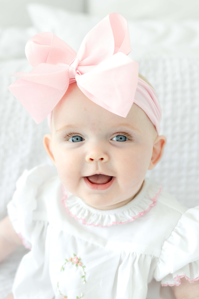 Baby with a pink bow smiling at the camera during a photography session in Dothan Alabama studio
