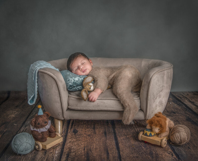 "Sleeping newborn nestled on a mini soft couch surrounded by charming vintage toys, captured in a nostalgic and whimsical fine art photography session in Ottawa."