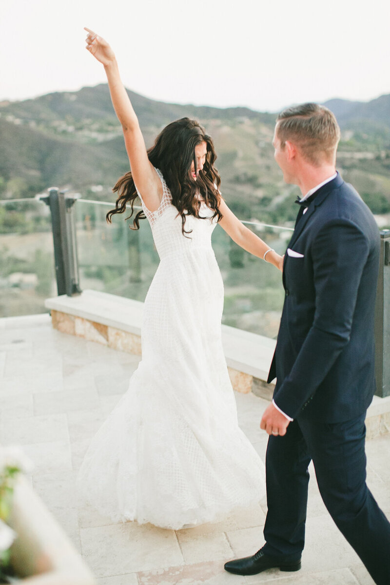 A happy bride raises her arms in excitement at a stunning outdoor venue, coordinated by WINK! Weddings for a dream destination wedding.