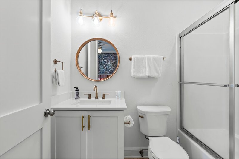 En-suite bathroom with round mirror, sleek white vanity, and brushed gold fixtures—designed for comfort and style during your beach vacation.