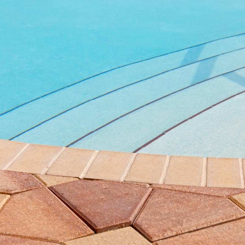 A pool withe white and black tile in the basin and earth tone stone around the pool.