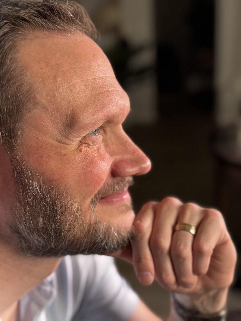 Thoughtful middle-aged man with a peaceful expression, gently smiling while resting his chin on his hand—symbolizing calm, clarity, and confidence. Ideal image for a Peace Coaching website promoting emotional wellness, stress relief, and personal growth