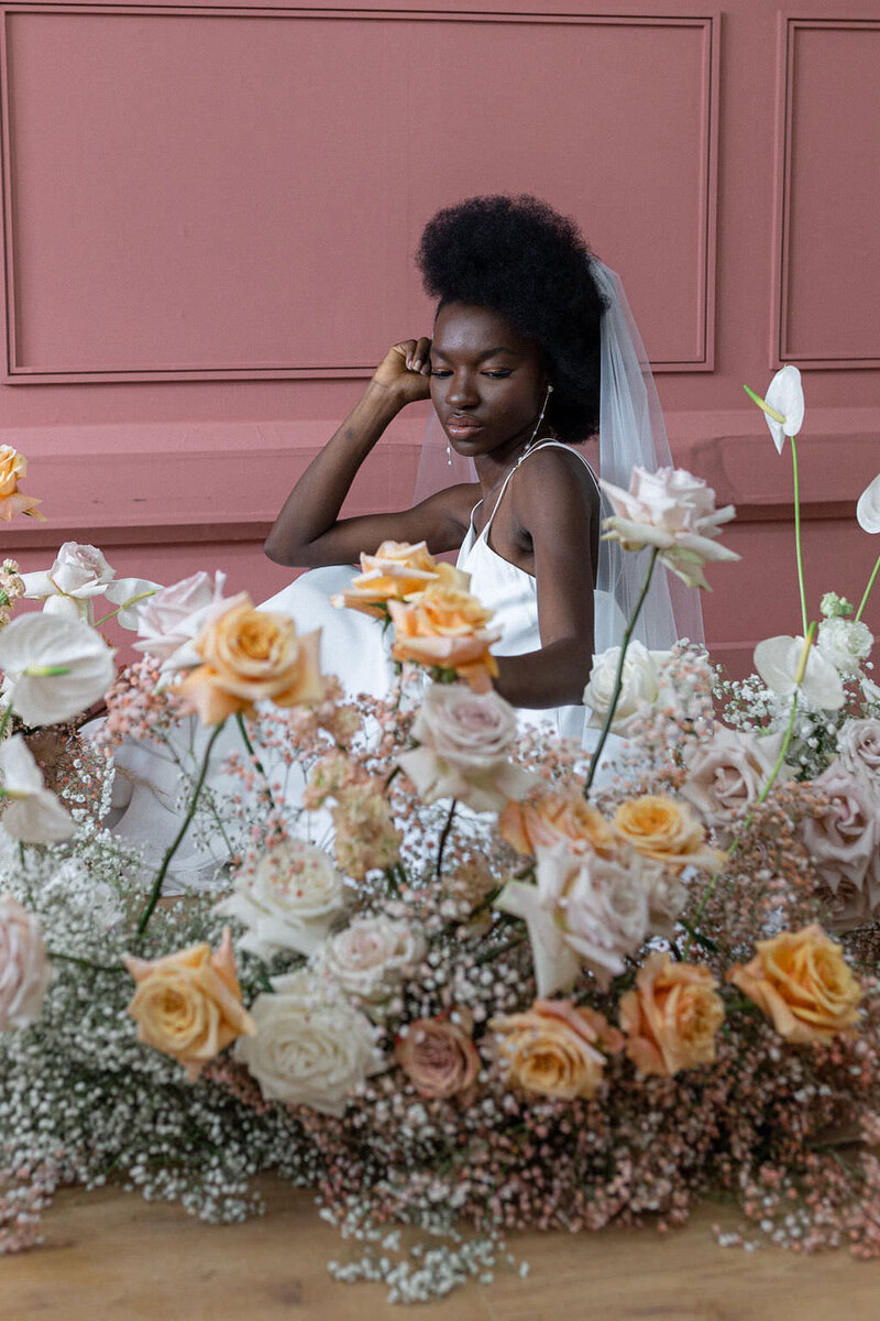 bride crouched down behind orange floral arrangement