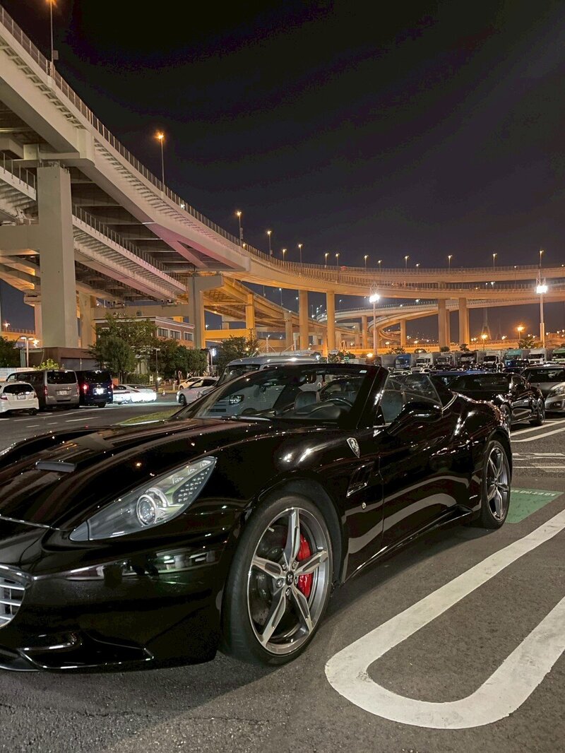 A sleek black Ferrari California glows under the lights at Tokyo’s iconic Daikoku Parking Area, capturing the essence of Japan’s elite night car culture with Tokyo Luxe Drive.
