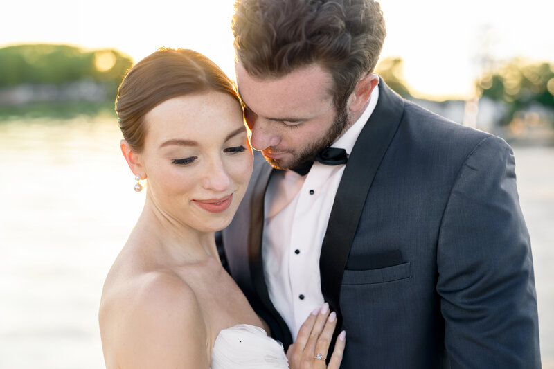 A couple in formal attire shares a tender moment. The woman wears a white strapless dress, and the man is in a dark suit and bow tie.