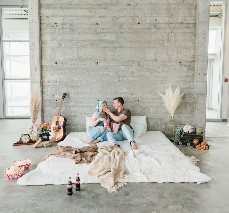 man and woman sitting on floor with man feeding woman popcorn