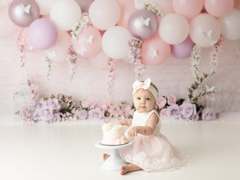 girl in pink dress sitting with cake for first birthday cake smash