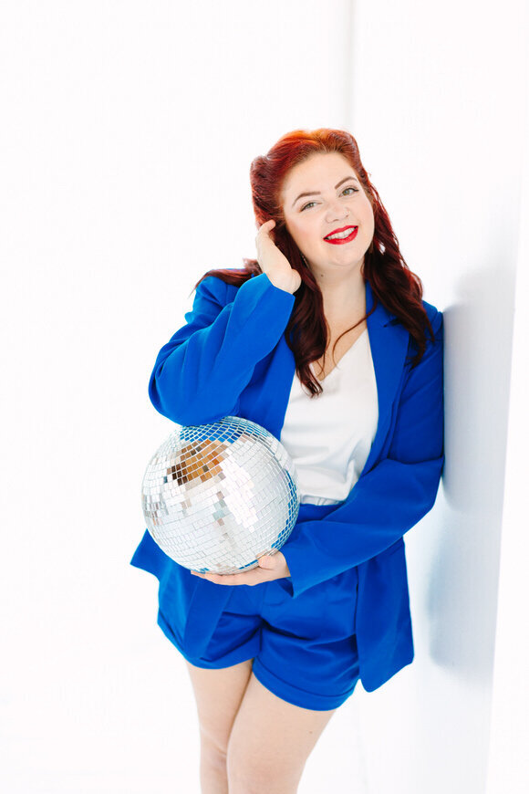 This image features Lelia Angelique, a North Carolina wedding photographer, captured in a bright, vibrant blue outfit while holding a disco ball. The portrait highlights her lively and dynamic personality, perfect for capturing romantic and vibrant wedding moments.