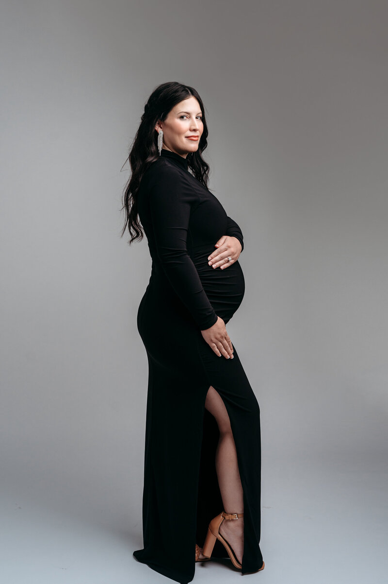 Pregnant mom in a black tight dress that gives her a beautiful silhouette for a portrait taken in a studio.