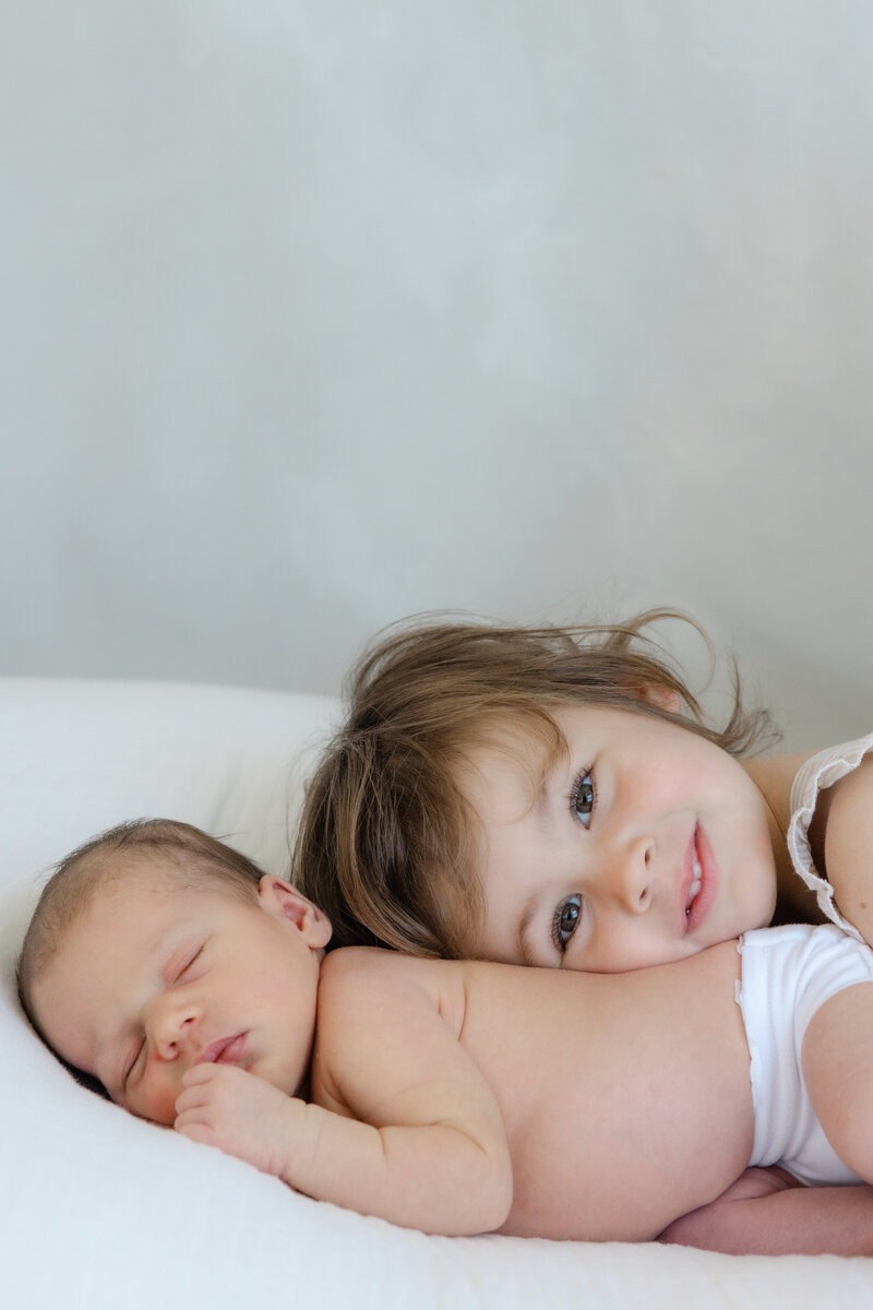 Candid photo of a newborn baby and toddler sibling lying together, captured in a natural light studio setting by Little Palm Photography in Marin County.